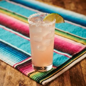 A paloma in a tall glass over ice with a salt rim and a lime wedge.